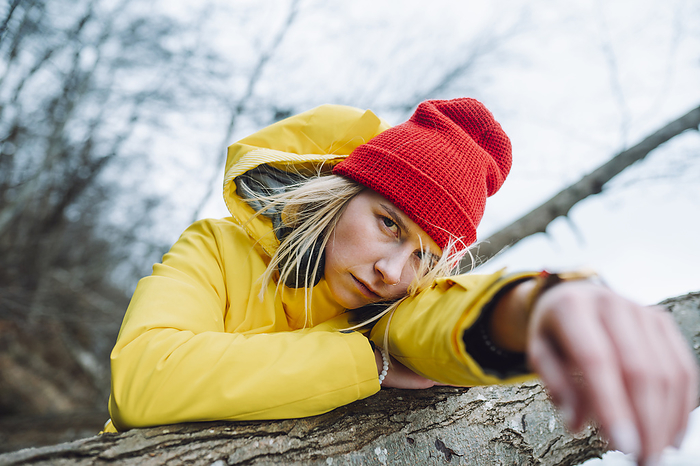 Serious young woman leaning on tree trunk
