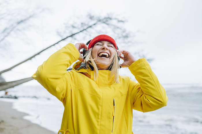 Cheerful woman wearing wireless headphones at beach