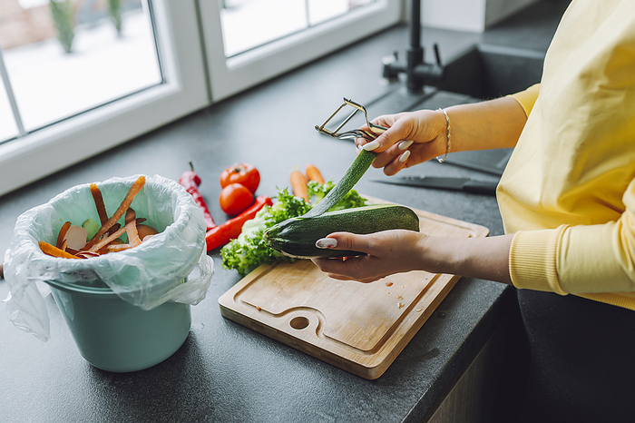 Hands of young woman peeling zucchini on kitchen counter at home