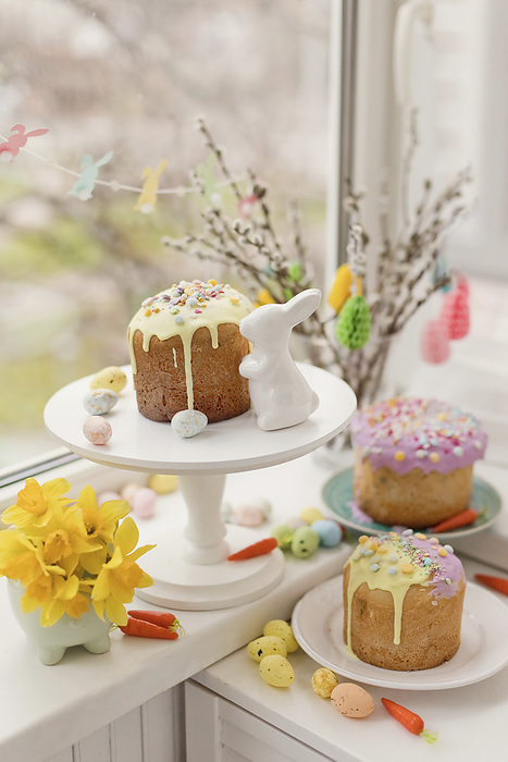 Cakes decorated with flowers and eggs near Easter bunny toy on window sill