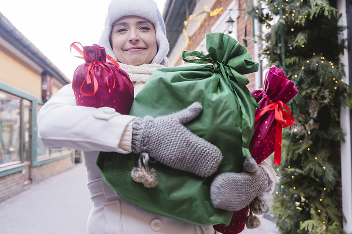 Smiling woman carrying gift bags at street in Christmas