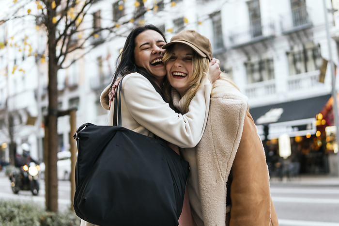 Happy woman laughing with friend standing at street in city
