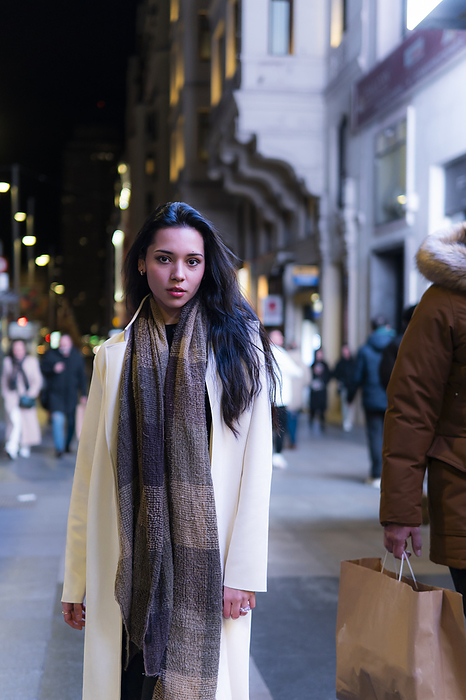 Young woman wearing scarf and overcoat standing in city at night