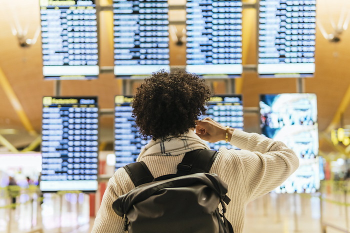 Man with curly hair looking at arrival departure board at airport