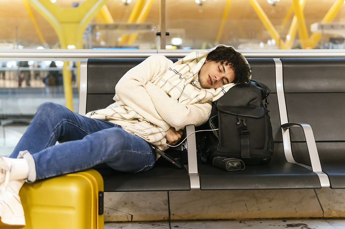 Young man taking nap leaning on backpack at airport lounge