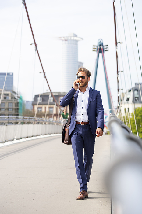 Businessman with smart phone walking on bridge in city