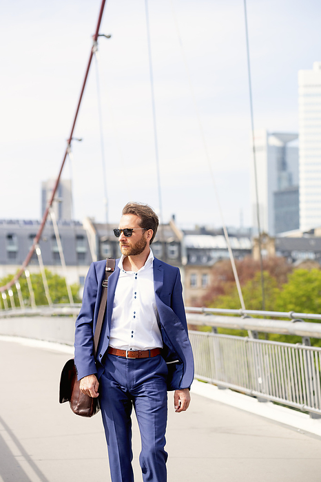 Businessman wearing sunglasses and walking on bridge in city