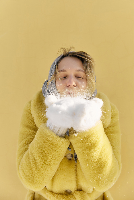 Young woman blowing on snow in front of yellow wall