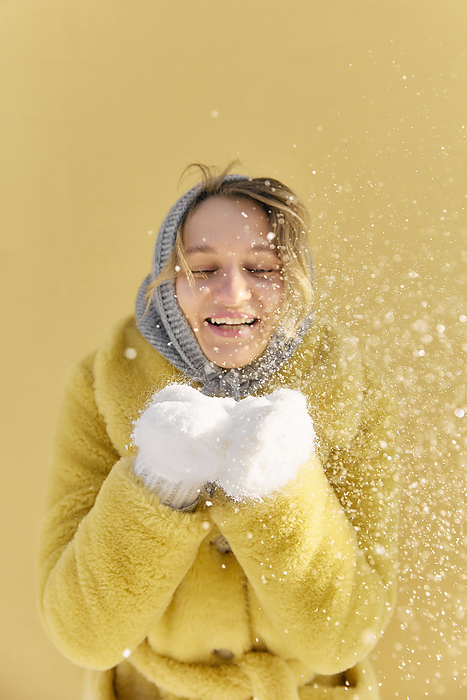 Happy young woman holding snow and standing in front of wall