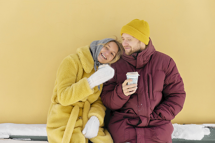 Happy couple enjoying coffee together in front of yellow wall