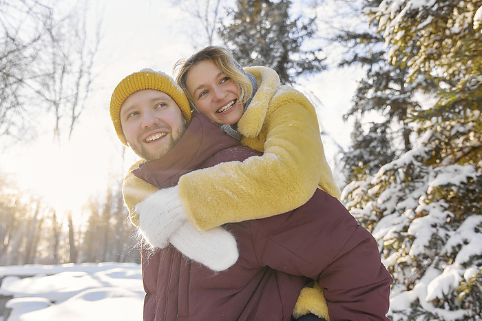 Smiling man giving piggyback ride to woman in winter forest