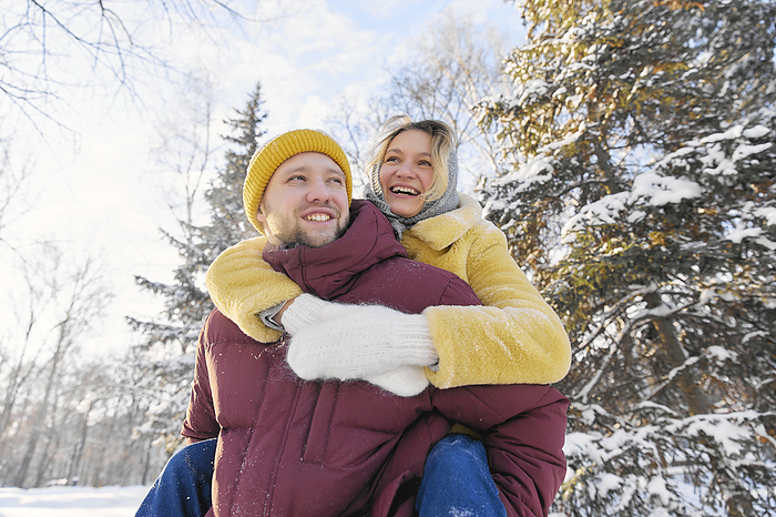 Happy man giving piggyback ride to young woman in winter forest