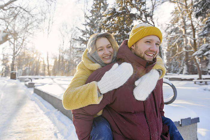 Happy man giving piggyback ride to woman in snow at winter forest
