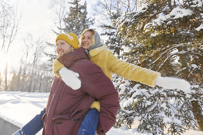Happy man giving piggyback ride to woman in winter forest