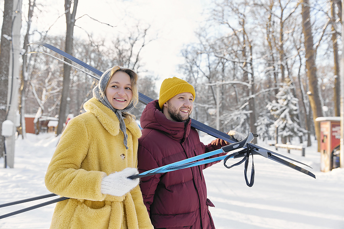 Happy man and woman with skis in winter forest