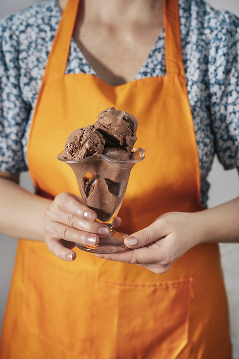 Woman wearing apron and holding chocolate ice cream in hand