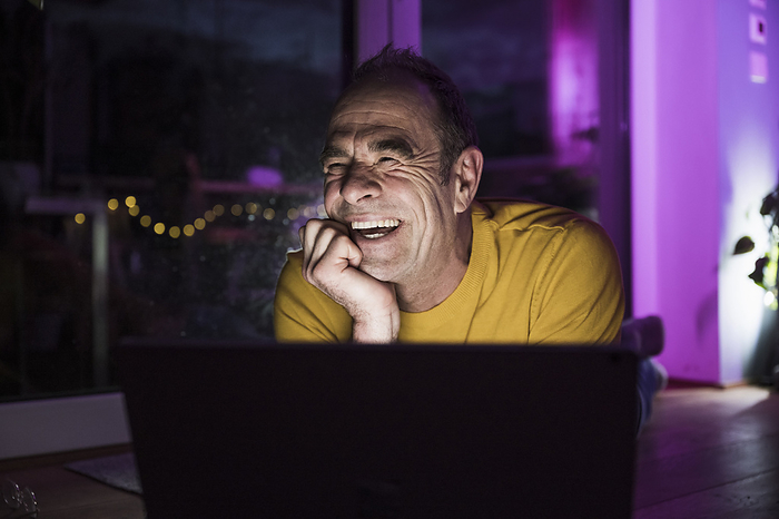 Mature man laughing near laptop at home