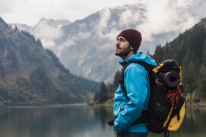 Young man with backpack standing in front of lake Vilsalpsee and mountains at Tyrol, Austria