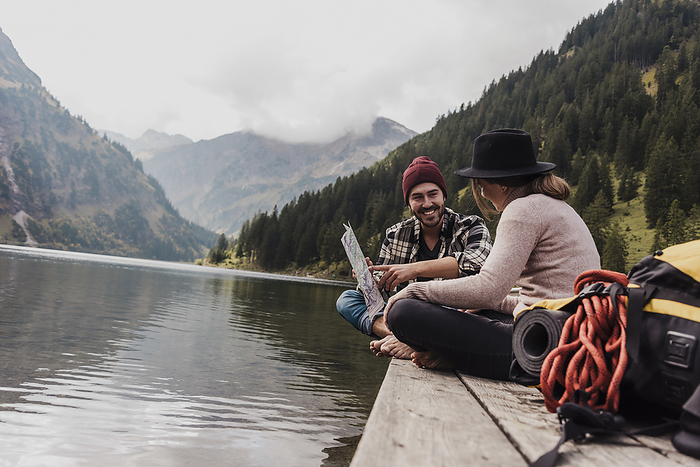 Happy young couple sitting with map on pier near lake Vilsalpsee and mountains at Tyrol, Austria