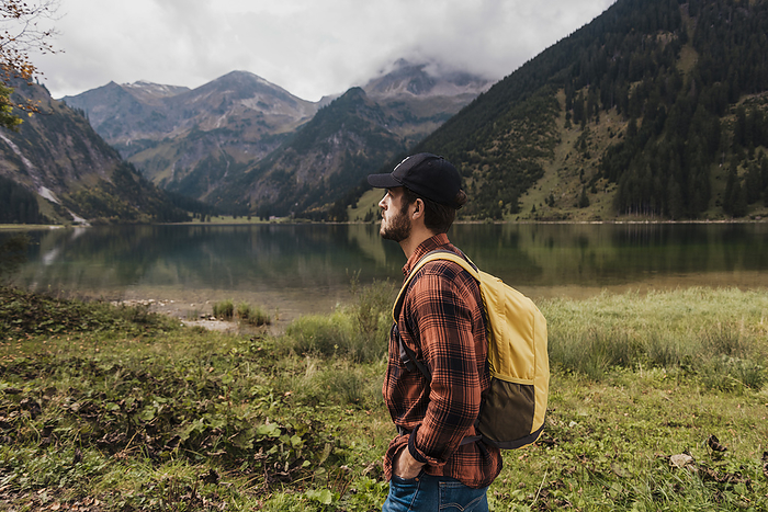 Thoughtful man with backpack standing in front of lake Vilsalpsee and mountains at Tyrol, Austria