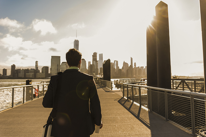 Businessman walking on bridge at sunset in city