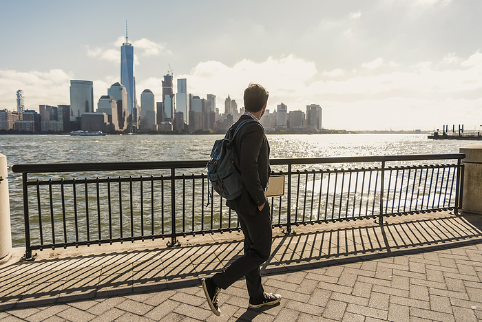 Businessman looking at skyline and walking on promenade in city