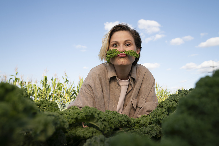 Playful farmer with kale leaves on lips in farm