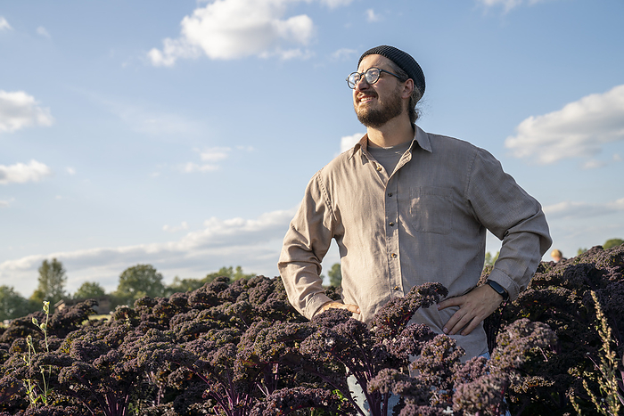Thoughtful farmer standing with arms akimbo in purple kale farm