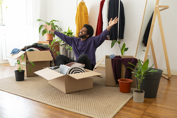 Cheerful young man with arms raised organizing and decluttering at home