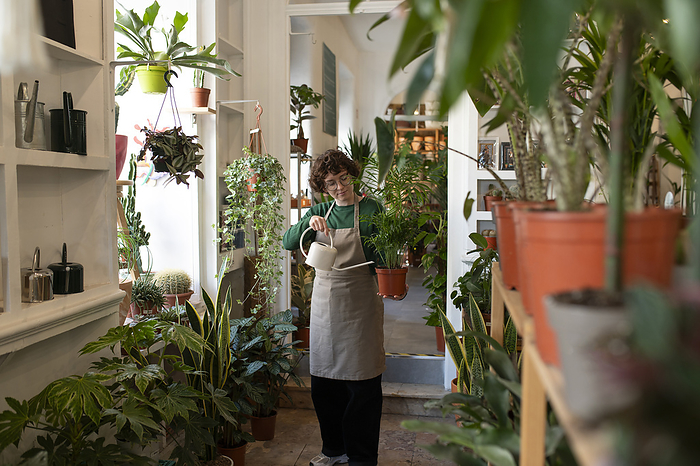 Shop owner wearing apron and watering plant at nursery