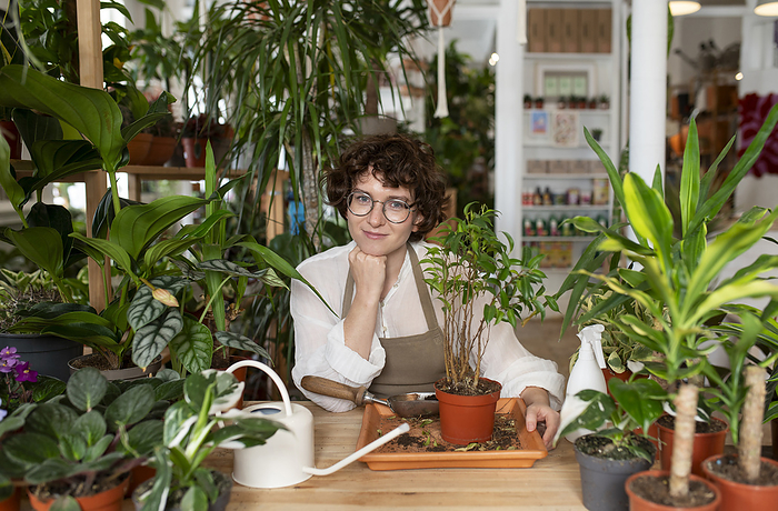 Smiling botanist potting plant at table in shop