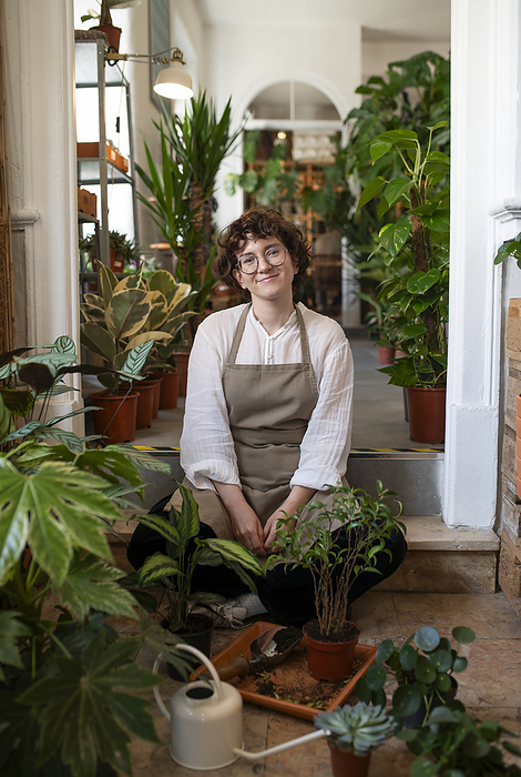 Smiling plant shop owner sitting with plants at nursery