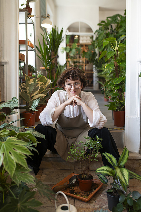 Smiling botanist leaning on elbows sitting amidst plants at nursery