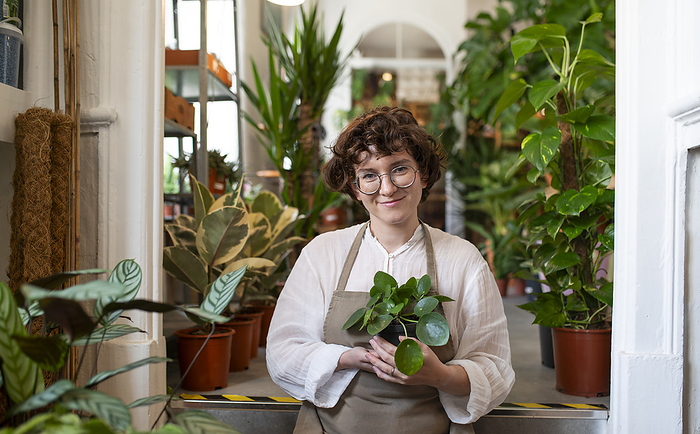 Smiling botanist holding potted plant at nursery