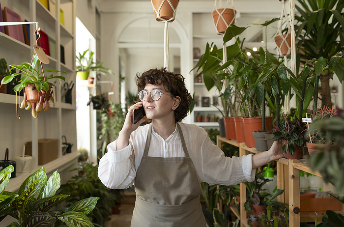Botanist talking on smart phone near potted plants at nursery
