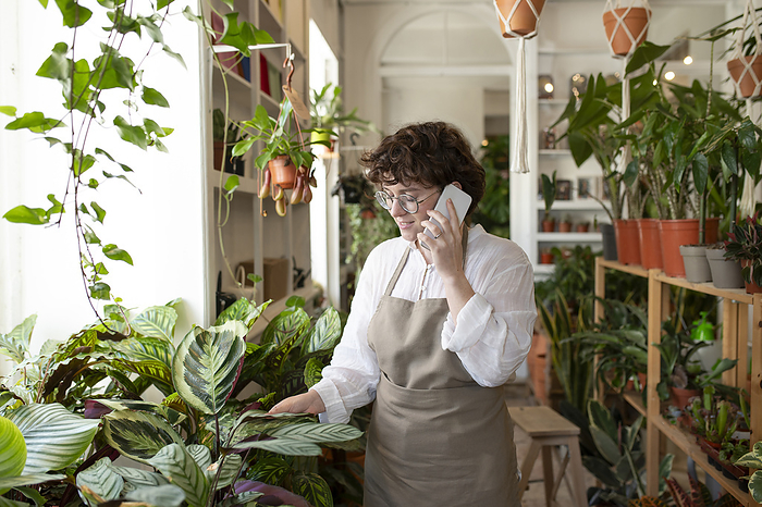Botanist talking on smart phone and examining plants at nursery