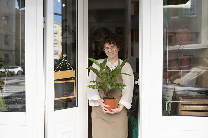 Smiling botanist holding plant at entrance of nursery