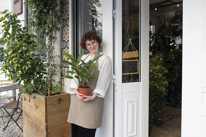 Smiling owner holding potted plant at nursery entrance