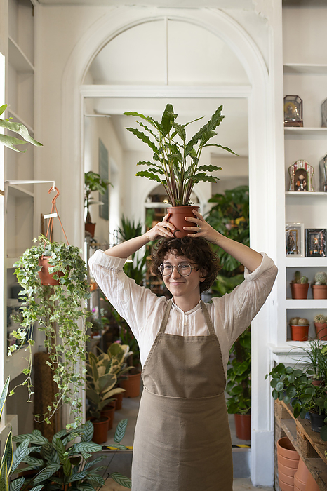 Smiling botanist holding potted plant overhead in nursery