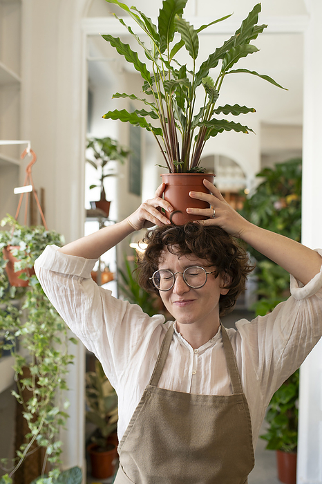Smiling botanist with eyes closed holding plant over head in nursery