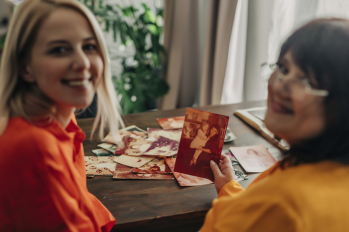Smiling mother and daughter with family photos at table