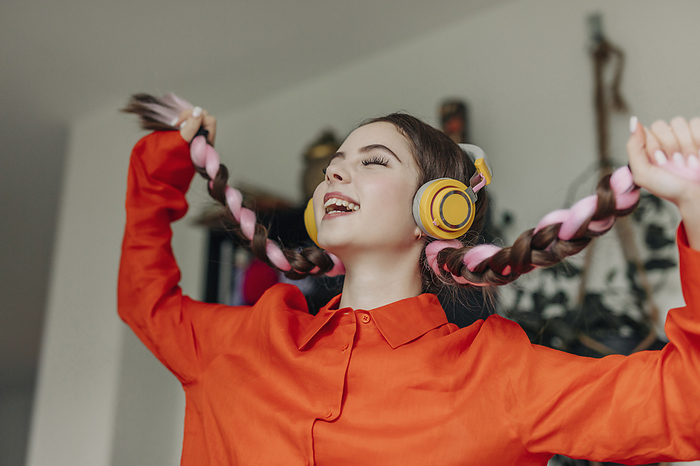 Happy young woman holding braids and listening to music at home