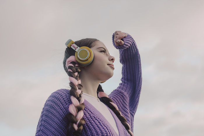 Young woman shielding eyes and listening to music through wireless headphones