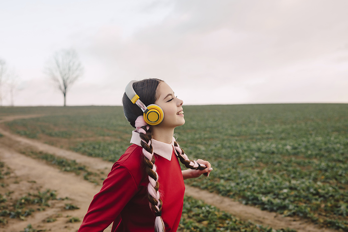 Happy young woman wearing wireless headphones and enjoying at field