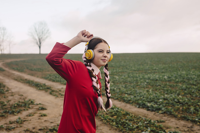 Smiling young woman wearing wireless headphones and enjoying at field