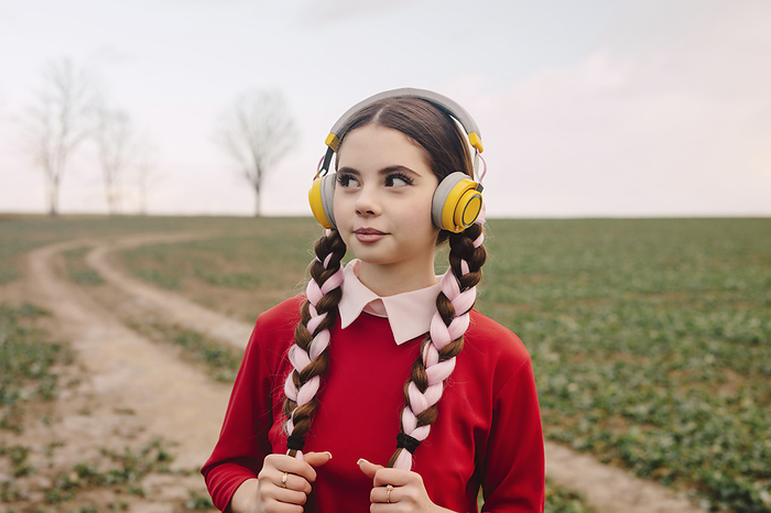 Young woman wearing wireless headphones and standing in field