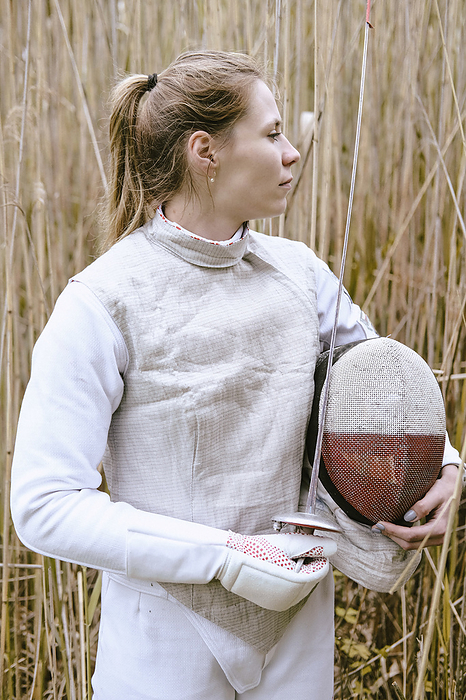 Fencer holding mask and foil standing amidst grass