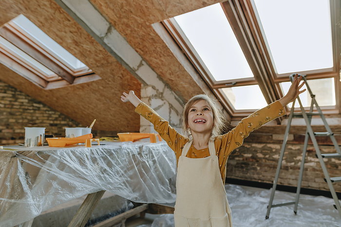 Cheerful girl standing with arms outstretched at house under construction