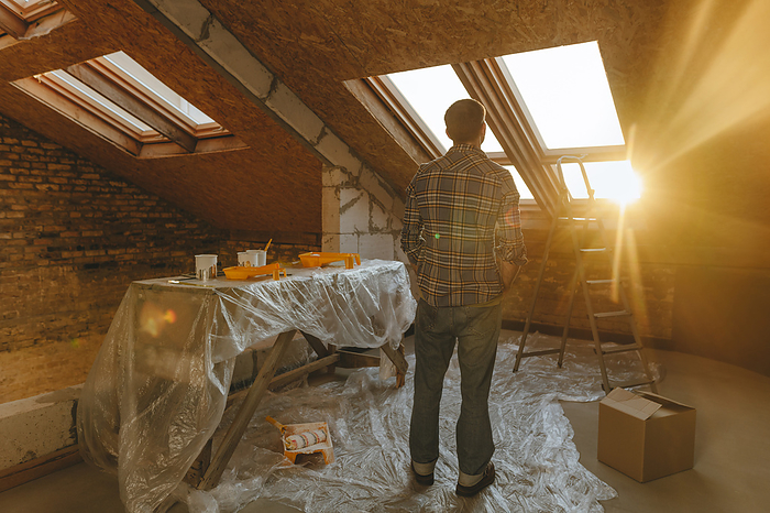 Man looking out of window standing in attic at home