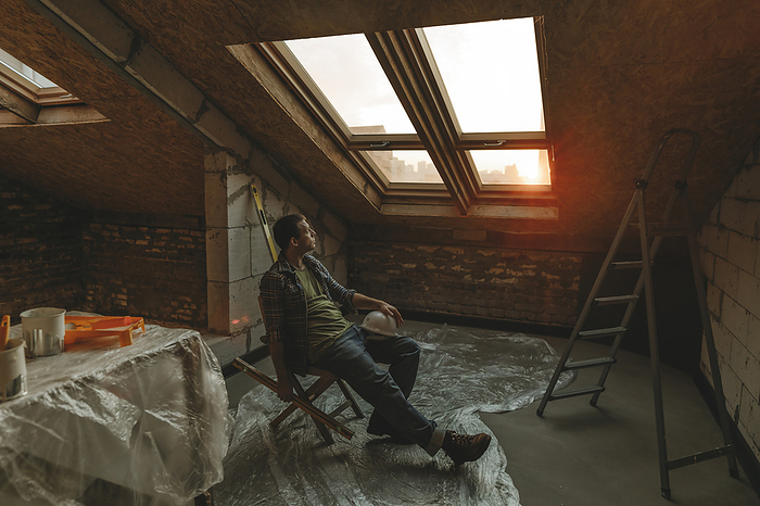 Construction worker sitting on table near window in room under renovation